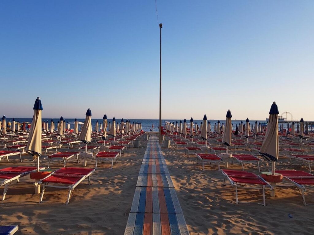 Rows of sun loungers and closed umbrellas on a beach at sunset, with the sea in the background