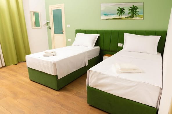 Two single beds with white linen and green headboards in a hotel room